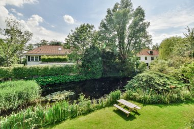 Bahçede piknik masası ve ortasında yemyeşil bitkiler ve ağaçlarla çevrili bir su kaynağı var.