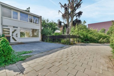 Önünde ağaç olan bir ev ve sokağın diğer tarafında da çalılar var.