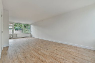 Ahşap döşeme ve duvarlarında beyaz boya olan boş bir oda. Köşesinde büyük bir pencere var.