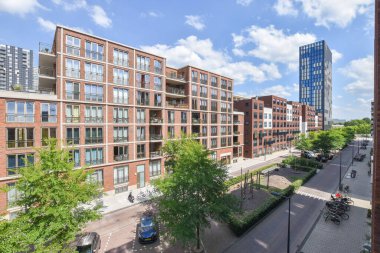Amsterdam, Netherlands - 10 April, 2021: a brick building on the side of a street with cars parked in front and trees lining the sidewalk behind it