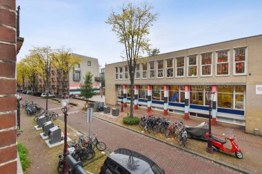Amsterdam, Netherlands - 10 April, 2021: a brick building on the side of a street with cars parked in front and trees lining the sidewalk behind it
