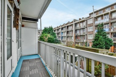 Ahşap döşemeli bir balkon ve apartmanın yan tarafında beyaz korkuluklar var.