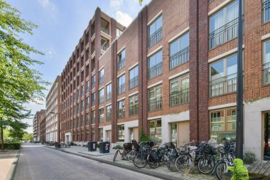 Amsterdam, Netherlands - 10 April, 2021: a brick building on the side of a street with cars parked in front and trees lining the sidewalk behind it