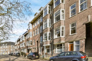 Yan tarafında arabalar ve arka tarafında binalar olan bir caddede bazı insanlar sokakta yürüyorlar.