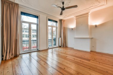 Boş bir oturma odası, ahşap döşeme ve sürgülü cam kapılar apartmanın balkon alanına açılıyor.