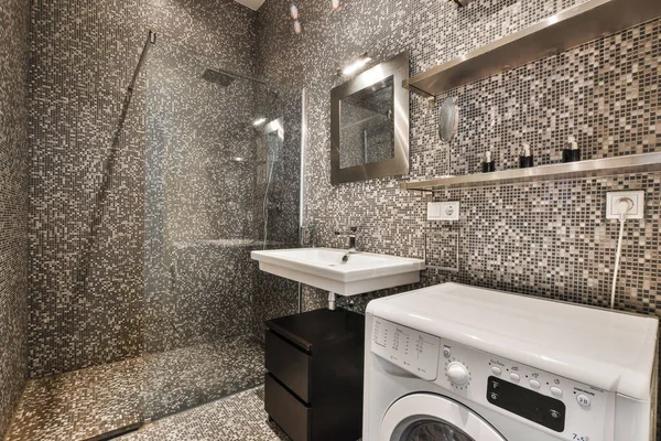 a laundry room with a washer and dryer in the shower stall, which is decorated with black and white mosaic tiles