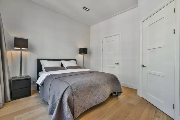 部屋には白い壁と木の床がある寝室には灰色の快適さがあるベッドがあります — ストック写真