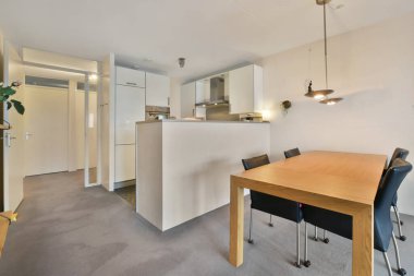 Bir yemek masası ve diğer duvarda açık bir mutfak olan bir odada sandalyeler beyazdır.
