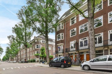 Amsterdam, Hollanda - 10 Nisan 2021: Kenarında arabalar olan bir şehir caddesi ve caddenin ortasında yürüyen insanlar