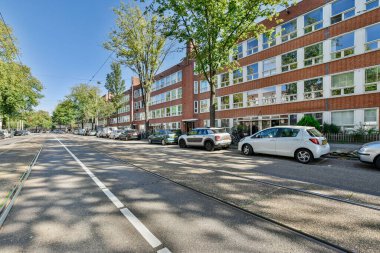 Amsterdam, Hollanda - 10 Nisan 2021: Kenarında arabalar ve sokağın ortasında ağaçlar olan bir şehir caddesi, sokağın karşısından görüldüğü gibi.