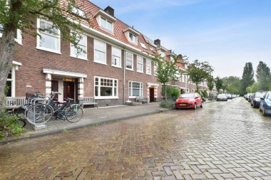 Amsterdam, Netherlands - 10 April, 2021: a brick building on the side of a street with cars parked in front and trees lining the sidewalk behind it