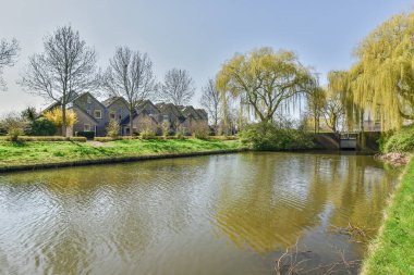Amsterdam, Hollanda - 10 Nisan 2021: Her iki tarafında evler ve ağaçlar olan bir mahallenin ortasında küçük bir nehir var.