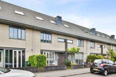 Bir apartman kompleksi, garaj yolunda arabalar ve caddenin her iki tarafında da binalar var, hepsi tuğlayla kaplı.