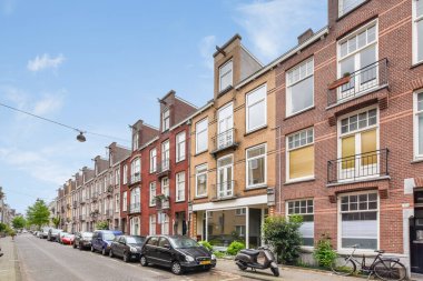 Kenarında arabalar, arka tarafında binalar olan bir şehir caddesi, açık mavi bir gökyüzü var.