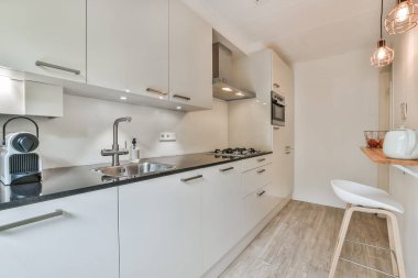 Modern bir mutfak, beyaz dolaplar ve lavabonun önündeki siyah tezgahlar paslanmaz çelikten.
