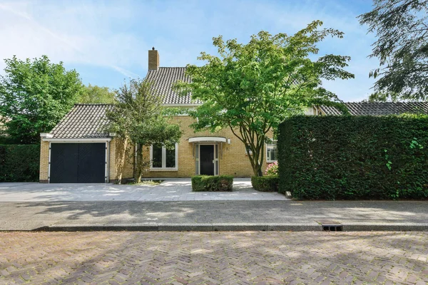 stock image a house that is in the middle of a driveway with trees and bushes on either side of the house there are two cars parked