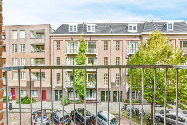 stock image Amsterdam, Netherlands - 10 April, 2021: some cars parked on the side of a street in front of a large brick building with many windows and bales