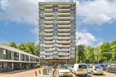 Amsterdam, Hollanda - 10 Nisan 2021: Önünde arabalar park edilmiş bir apartman ve insanlar kaldırımdan park alanına doğru yürüyorlar.