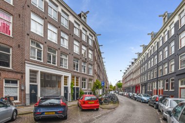 Amsterdam, Netherlands - 10 April, 2021: some cars parked on the side of a street in an urban area with bricked buildings and blue sky above