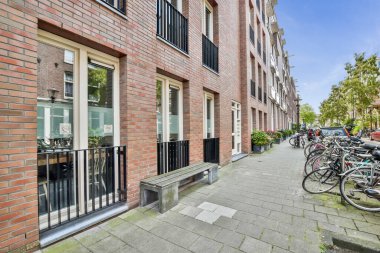 Amsterdam, Hollanda - 10 Nisan 2021: Bazı bisikletler siyah kapılı ve pencereli kırmızı tuğlalı bir binanın önündeki caddenin kenarına park ettiler