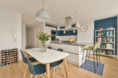 Mavi duvarları, ahşap döşemeleri ve her iki tarafında beyaz dolapları olan bir evde mutfak ve yemek odası.