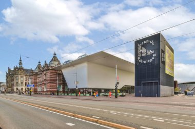 Amsterdam, Hollanda - 10 Nisan 2021: Büyük binanın önünde yol kenarında yürüyen insanlar ve binaları olan boş bir şehir caddesi