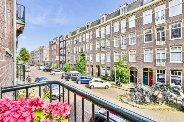 Amsterdam, Hollanda - 10 Nisan 2021: Park etmiş arabaların ve çiçeklerin bulunduğu bir sokak - fotoğrafın sol tarafında pencereli bir alan