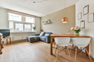 Odanın ortasında küçük bir yemek masası da dahil olmak üzere ahşap döşemeli ve beyaz duvarlı bir oturma odası.