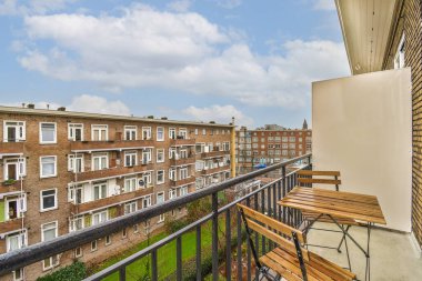 Balkonunda banklar ve masalar olan bir dış alan aşağıdaki sokağa bakıyor, arka planda binalar var.