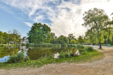 Amsterdam, Hollanda - 10 Nisan 2021: Her iki tarafında ağaçlar ve çalılarla dolu bir parkın ortasında mavi bir gökyüzü var.