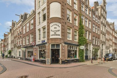 Amsterdam, Hollanda - 10 Nisan 2021: Tuğlalı bir bina, sokak ortasında arabaları park edilmiş ve insanlar yanından geçiyor.
