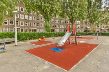 Amsterdam, Hollanda - 10 Nisan 2021: Bir tarafta kaydırak, diğer tarafta çocuklar için oyun alanı olan bir apartman kompleksinin ortasında bir oyun alanı