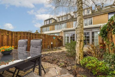 Arka bahçesinde bir masa, sandalyeler ve çiçekler çitli arka bahçenin önünde.