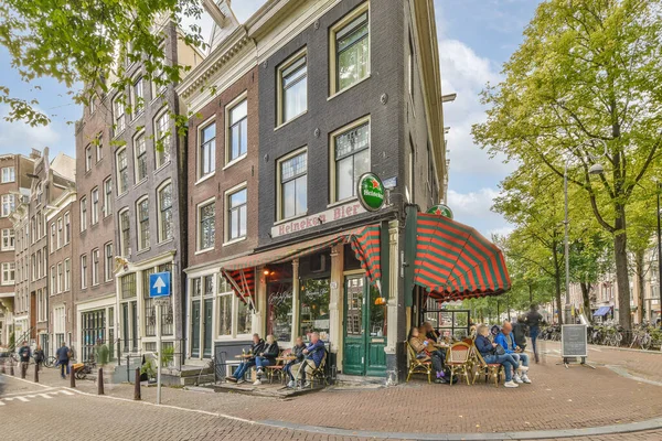 stock image people sitting at tables in front of a restaurant on a bricked street lined with trees and parked cars along the sidewalk