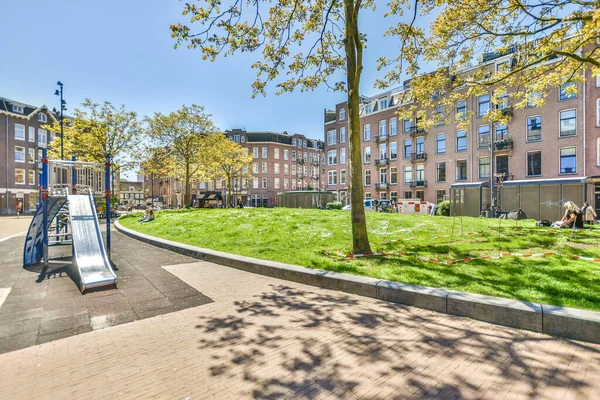 stock image Amsterdam, Netherlands - 10 April, 2021: a park with benches and trees in the middle part of the city, on a sunny day there is an empty street