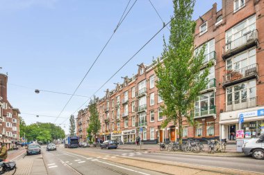 Amsterdam, Hollanda - 10 Nisan 2021: Kenarında arabaları olan bir şehir caddesi ve caddenin ortasında yürüyen insanlar