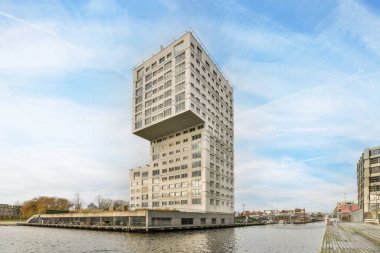 Amsterdam, Hollanda - 10 Nisan 2021: Arka planda binalar ve üzerinde mavi gökyüzü olan bir su kütlesi üzerinde yüksek bir bina