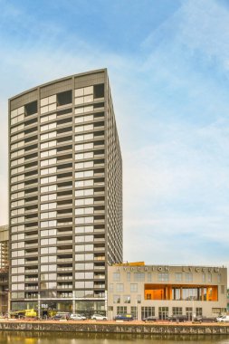 Amsterdam, Hollanda - 10 Nisan 2021: Deniz kenarında bir ofis binası önünde tekneler ve nehir boyunca yürüyen insanlar