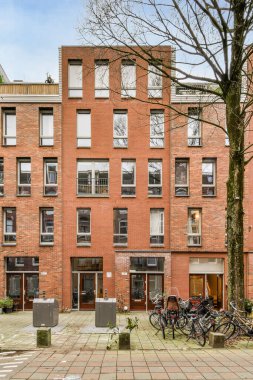 Önünde ve yanındaki kaldırımda bisikletleri olan tuğla bina yaprakları olmayan bir ağaçtır.