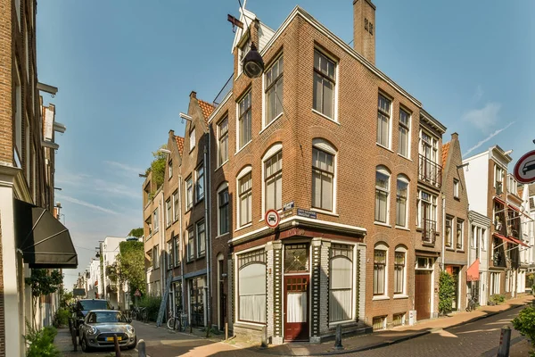 stock image Amsterdam, Netherlands - 10 April, 2021: a brick building in the middle of a street with cars parked on both sides and people walking down the street