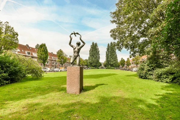 stock image Amsterdam, Netherlands - 10 April, 2021: a statue in the middle of a green lawn with trees and houses in the background on a bright sunny day