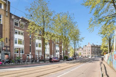 Yolun kenarına park etmiş arabaları olan bir şehir caddesi ve yolda yürüyen insanlar.