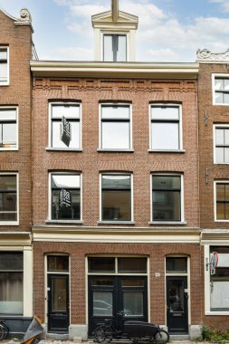 Amsterdam, Hollanda - 10 Nisan 2021: Tepesinde saat olan tuğla bir bina ve önünde yan yana park edilmiş iki araba