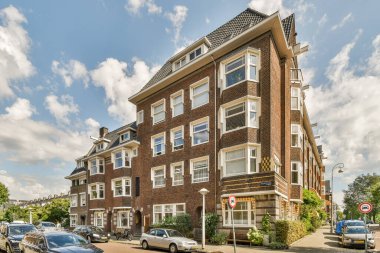 Amsterdam, Hollanda - 10 Nisan 2021: Arabaların olduğu bir apartman ve arka plandaki bazı binalar bulutlu gökyüzü.
