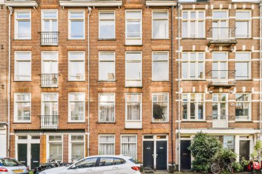 Amsterdam, Netherlands - 10 April, 2021: some cars parked in front of an apartment building with many windows and bales on the side of the street