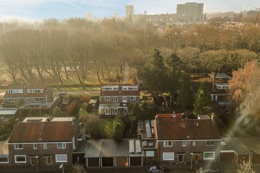 Amsterdam, Hollanda - 10 Nisan 2021: sisli bir günde arka planda ağaçlar ve binalar olan bazı evler bir uçak penceresinden görülebiliyor.