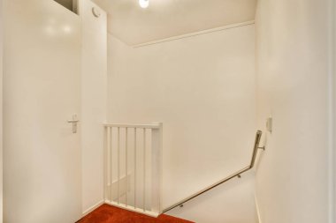 Kırmızı halılı beyaz bir oda ve duvarın sol tarafında demir korkuluklar var.