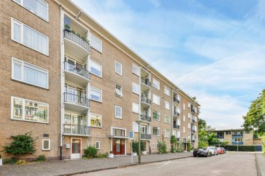 Amsterdam, Hollanda - 10 Nisan 2021: Hollanda 'da bir apartman kompleksi. Arabalar caddeye park edilmiş ve ağaçlar binanın yanında asılı.