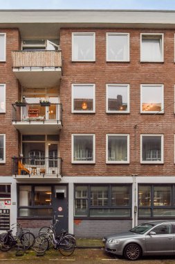 Amsterdam, Hollanda - 10 Nisan 2021: bitişiğinde bisikletleri olan bir apartman ve binanın önüne park edilmiş iki araba