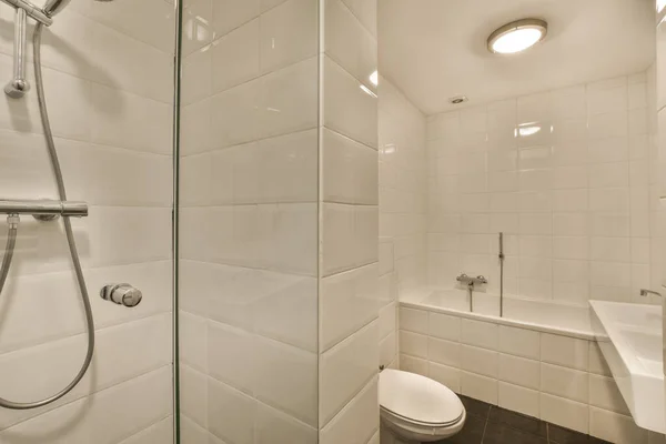 浴槽の角にあるトイレの横には白いタイルと黒い床のついたモダンなバスルームがあります — ストック写真